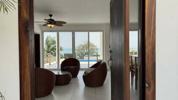 Una porta aperta su una stanza con ventilatore a soffitto, mobili in vimini e vista sul mare.