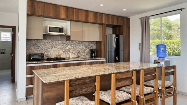 Eine moderne Küche mit Granit Arbeitsplatte, Holzschränken, einem Edelstahl-Kühlschrank und einer eingebauten Mikrowelle.