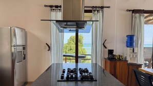 Een keuken met uitzicht op zee, een koelkast, een waterdispenser en een eethoek met een tafel en stoelen.