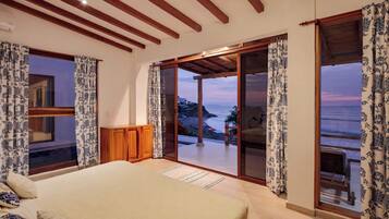 Quarto com uma cama grande, vigas de madeira e vista para o mar.