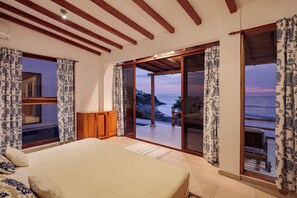 A bedroom with a large bed, wooden beams, and a view of the sea.
