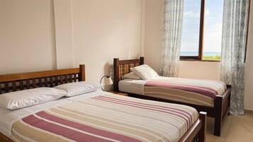 Quarto com duas camas de solteiro, janela com cortinas e vista para o mar.