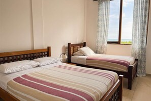 A bedroom with two single beds, a window with curtains, and a view of the sea.