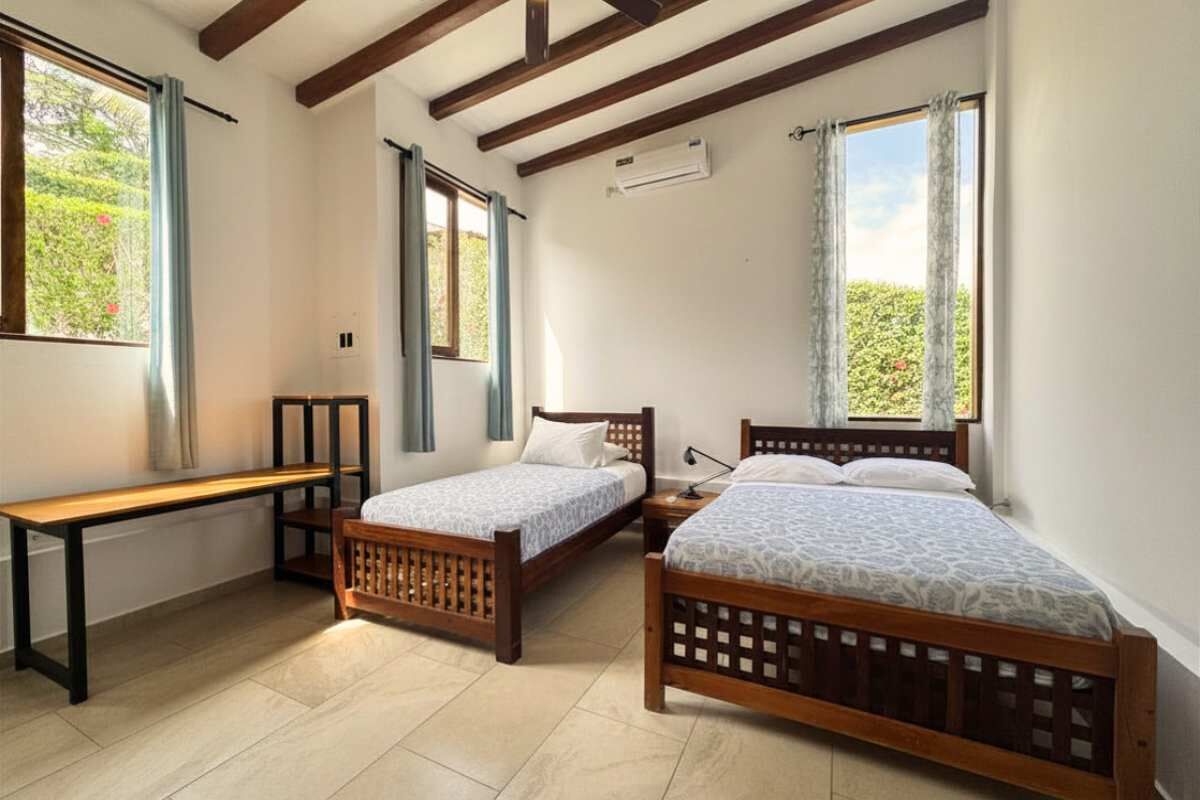 Un dormitorio con dos camas de madera, un banco y una ventana con cortinas.