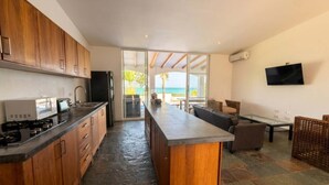 A modern kitchen with a central island, wooden cabinets, and a view to the outdoors. - Beachfront | Pool With Views | Family & Friends (Camarones)