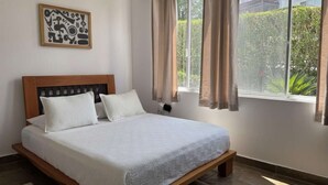 A bedroom with a bed, a window with curtains, a wall-mounted light, and a framed abstract artwork. - Beachfront | Pool With Views | Family & Friends (Camarones)