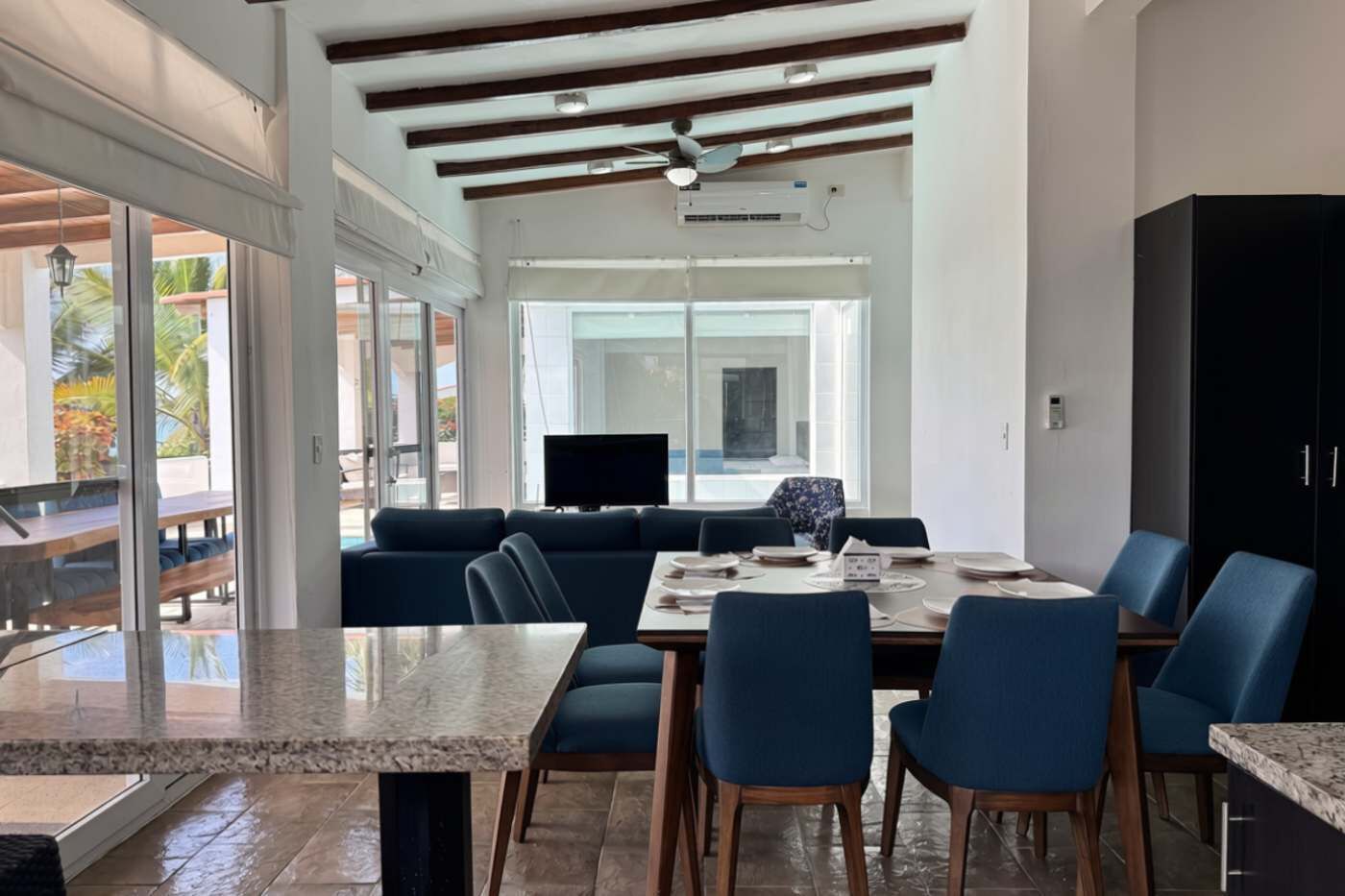 A spacious dining area with a large table, blue chairs, and a ceiling fan.