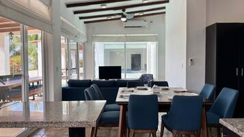 A spacious dining area with a large table, blue chairs, and a ceiling fan.