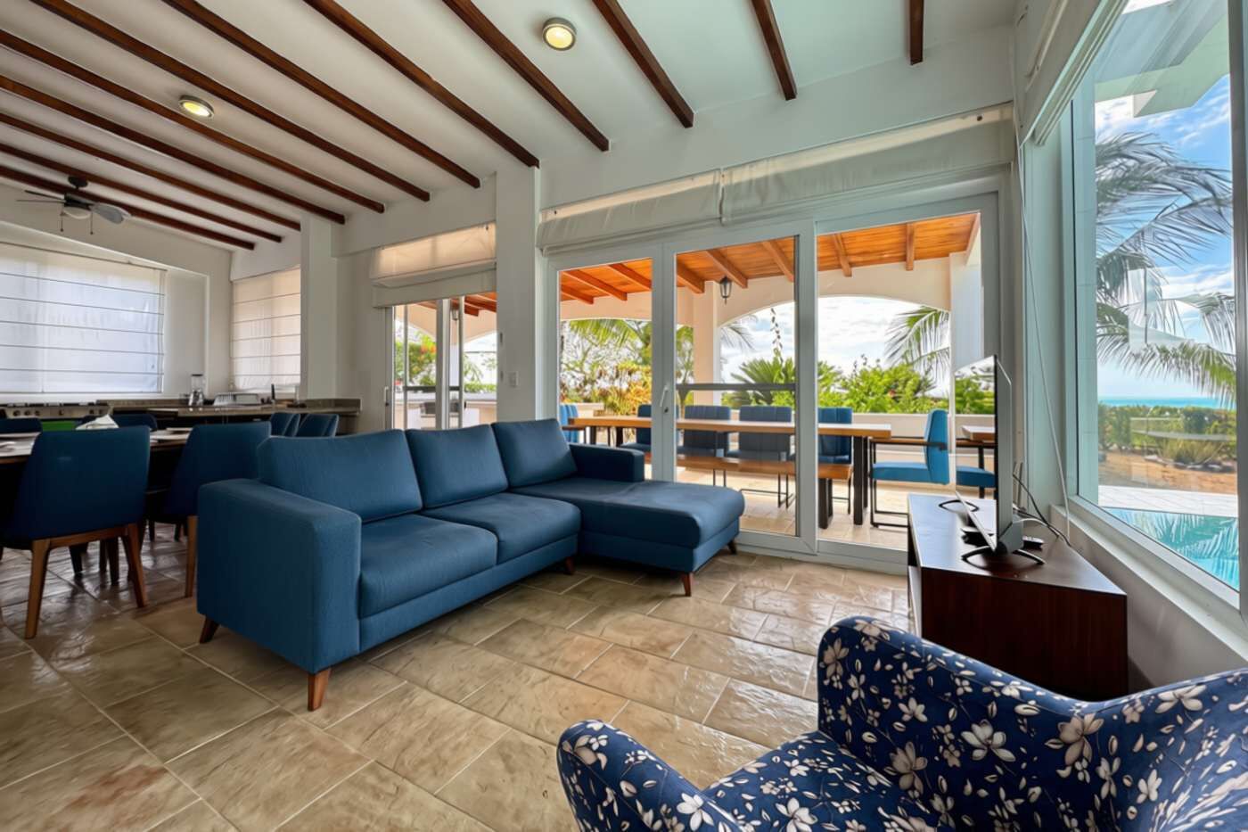 Ein moderner Lounge-Bereich mit einer Eckcouch, einem gemusterten Sessel und einem Essbereich mit Tischen und Stühlen.