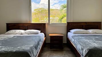 Una habitación con dos camas, una mesita de noche de madera y una ventana con vista a árboles.