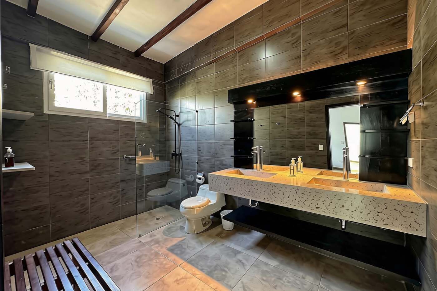 Un baño moderno con ducha, inodoro y un amplio tocador con espejo.
