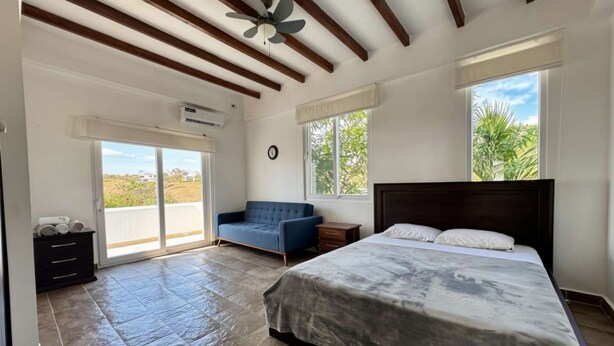 Ein Schlafzimmer mit Bett, einer Couch, einem Deckenventilator und Blick ins Grüne.