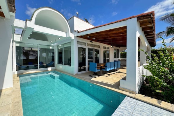 A modern house with a swimming pool, outdoor seating, and a covered patio area.