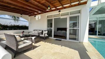 A covered outdoor area with a pool, a sofa set, and a bed with sliding glass doors.