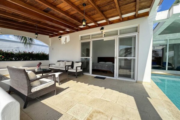 A covered outdoor area with a pool, a sofa set, and a bed with sliding glass doors.
