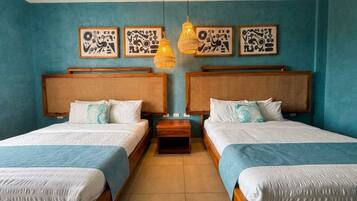 A room with two beds, each with a wooden headboard and white bedding. There are two wall-mounted light fixtures and three framed artworks above the beds.