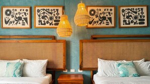 Ein Hotelzimmer mit zwei Betten, einem kleinen Holz-Nachttisch und drei an der Wand befestigten Kunstwerken.