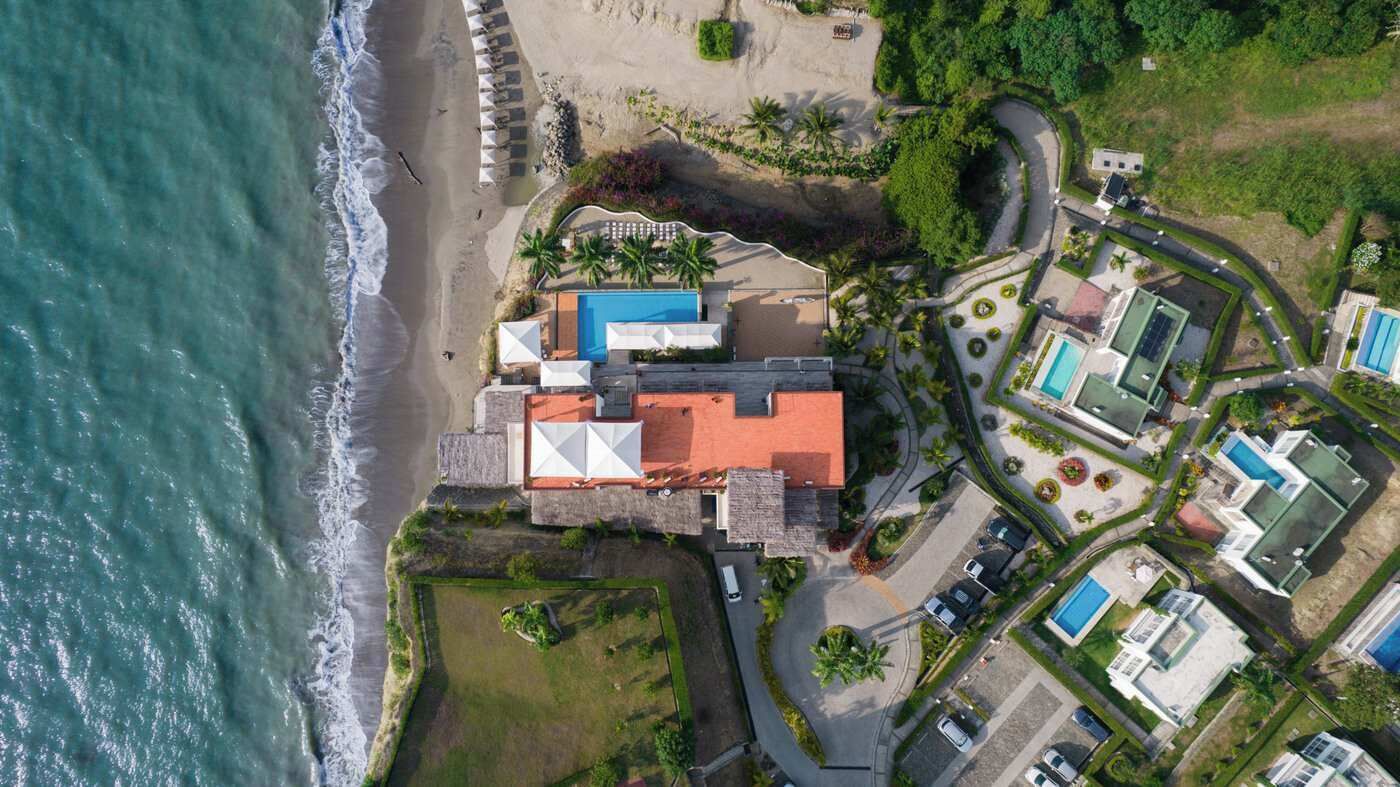 Luchtbeeld van een kusthotel met een zwembad, meerdere gastenkamers en een strand.