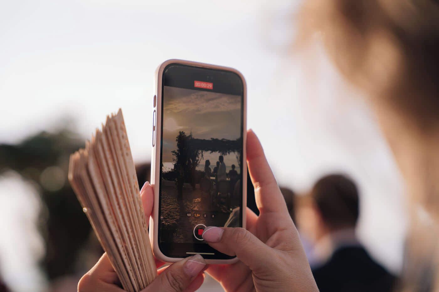 A person holding a smartphone with a camera interface, displaying a photo of a beach scene.