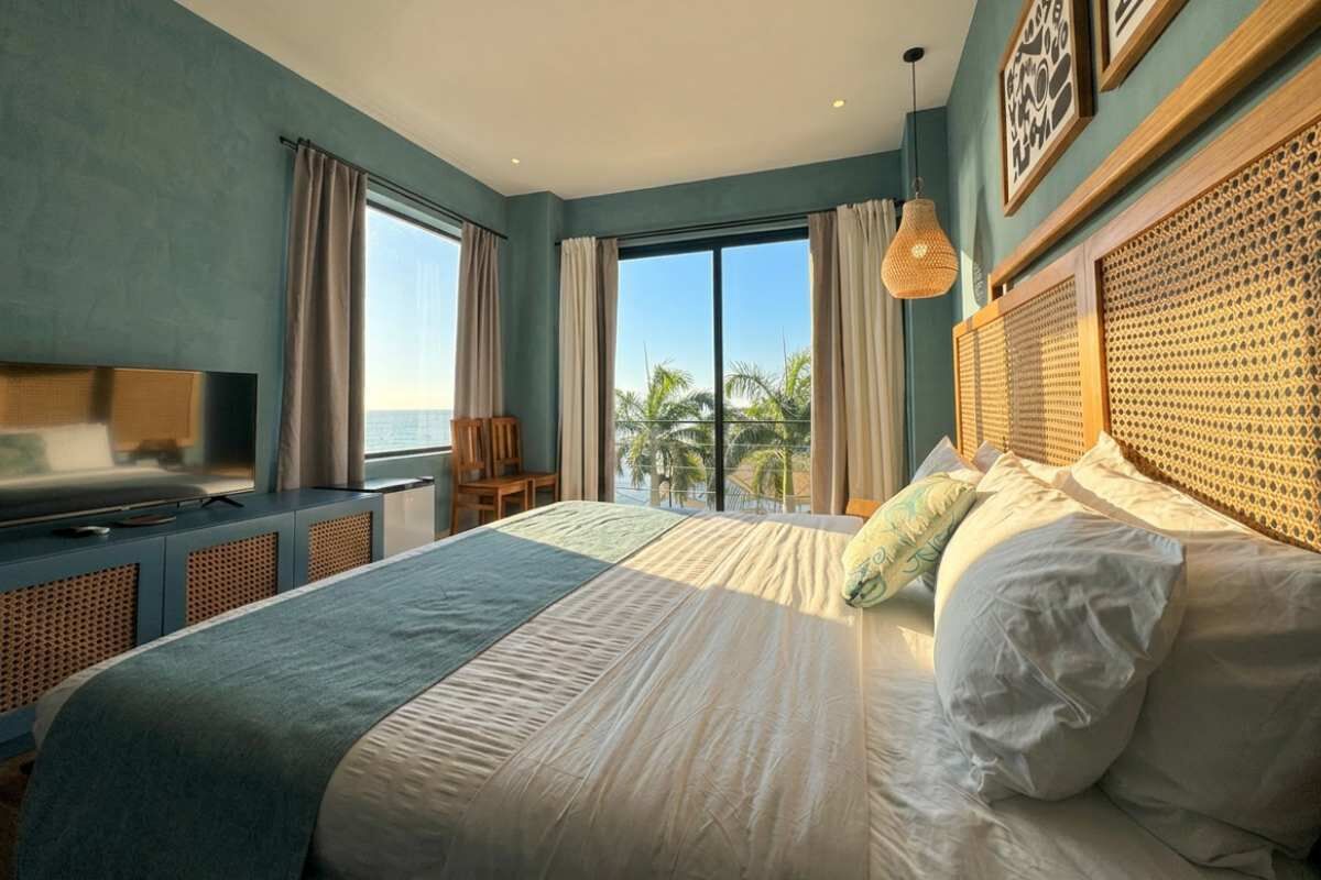 A bedroom with a large bed, a television, and a view of the ocean.