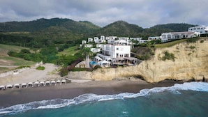 A coastal property with multiple white buildings, a beach, and a cliff.