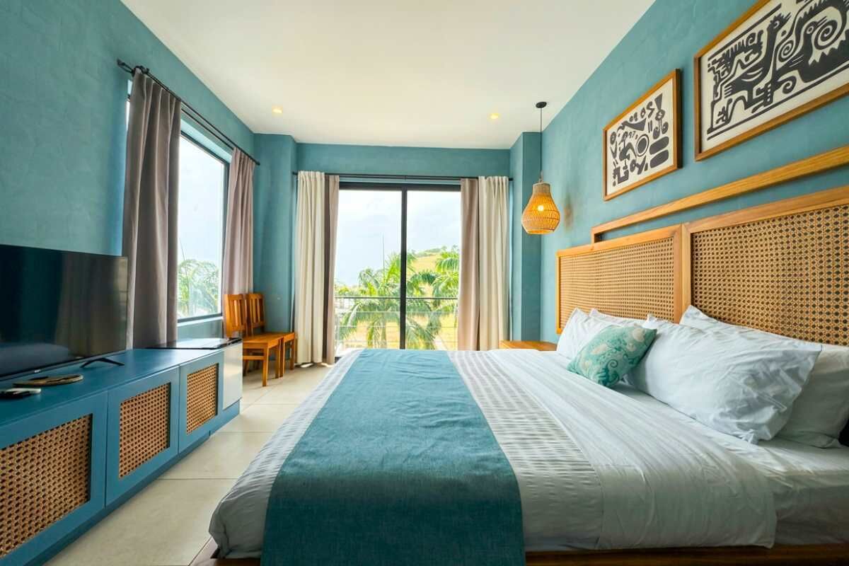 Un dormitorio con una cama grande, un televisor sobre un mueble azul y obras de arte en la pared.