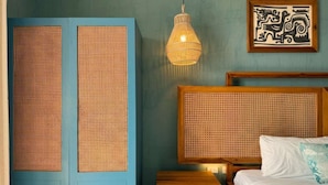 A room with a bed, a wooden nightstand, a woven wall panel, a hanging light fixture, and a framed artwork.