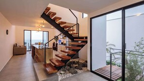 A modern interior with a wooden staircase, a kitchen area, and a view through a glass door. - Jama Campay Villas by Otium (Camarones)