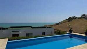 A modern pool with a clear view of the ocean and a hilly landscape in the background. - Jama Campay Villas by Otium (Camarones)