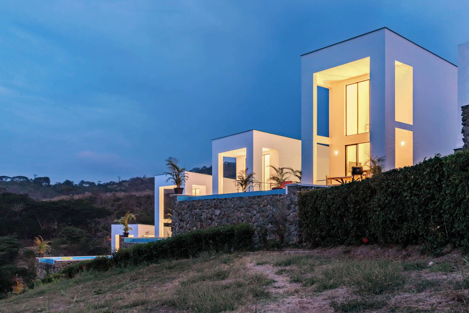 Una casa moderna de varios pisos con amplios ventanales y un muro de piedra en la base.
