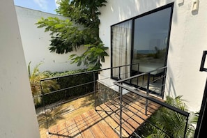 Un balcon extérieur moderne avec une terrasse en bois, une rambarde en métal et une vue sur l’océan.