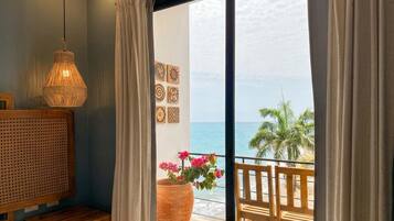 A room with a bed, a large potted plant, a hanging light fixture, and a view of the ocean.