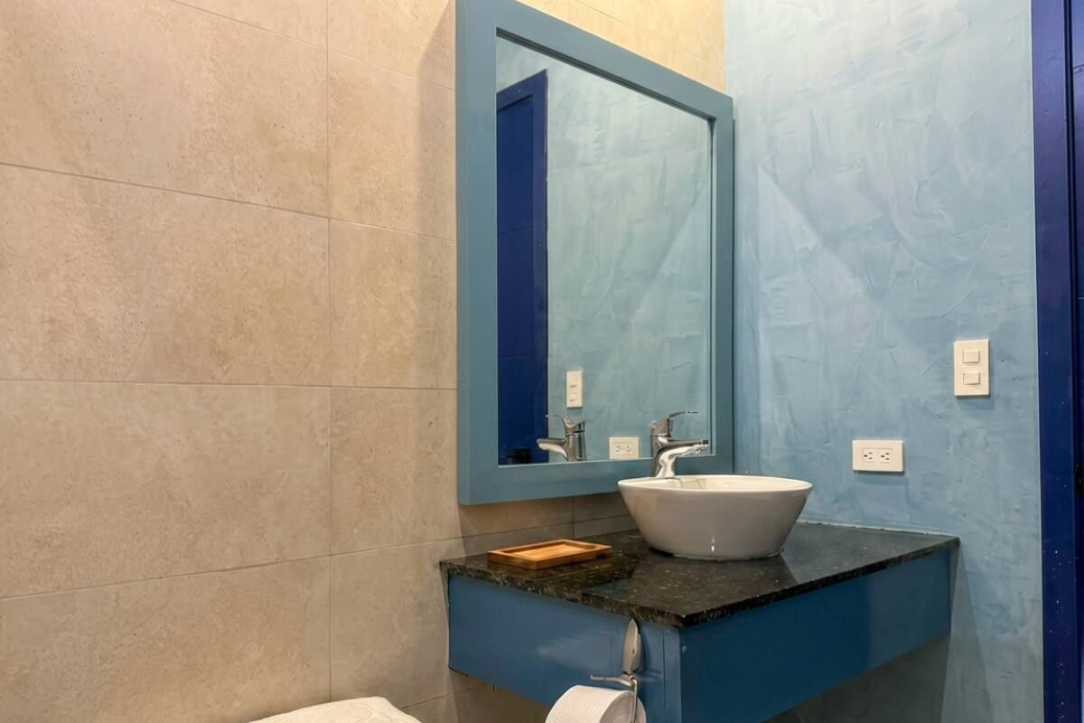 Un baño con pared azul, lavamanos blanco y espejo encima.