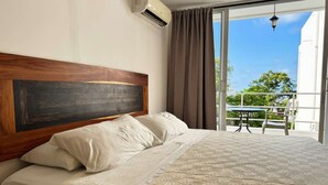 Een hotelkamer met een groot bed, een houten hoofdeinde, een balkon met een tafel en stoelen, en uitzicht op groen.