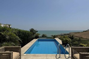 Une piscine rectangulaire offrant une vue dégagée sur l’océan en arrière-plan.