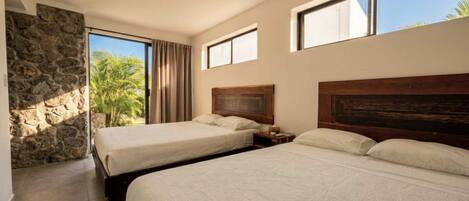 A hotel room with two beds, a stone wall, and a view of palm trees.
