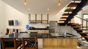 A modern kitchen with a central island, wooden chairs, a dining table, and a staircase with wooden steps. - Oceanfront Villa | Private Pool | Jama Campay (Camarones)