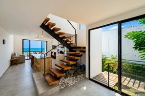 A modern interior with a wooden staircase leading to a balcony overlooking a garden.