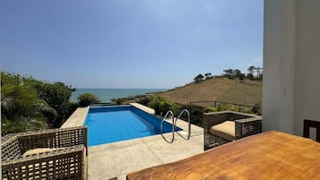 A pool with a view of the sea, wicker furniture, and a wooden table.