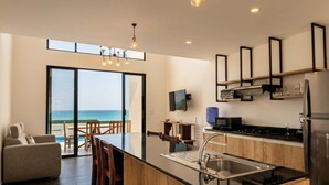 A modern kitchen with a large island, a dining area with a view of the ocean, and a flat-screen TV mounted on the wall. - Oceanfront Villa | Private Pool | Jama Campay (Camarones)