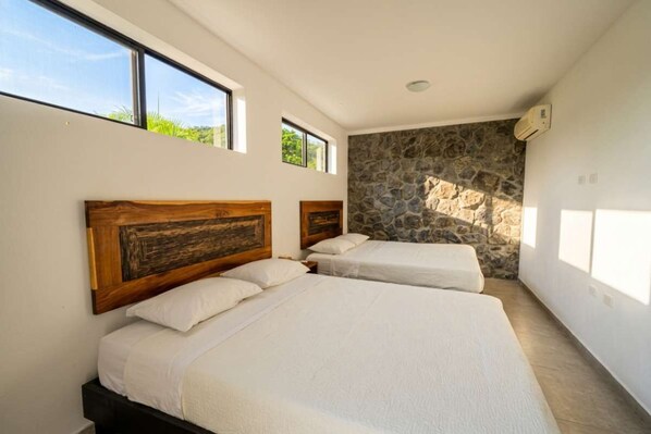 A bedroom with two beds, a stone wall, and large windows.