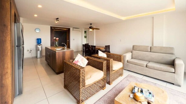 Ein modernes Wohnzimmer mit einer Couch, zwei Korbstühlen, einem Couchtisch und einem Essbereich mit Stühlen und einem Tisch.