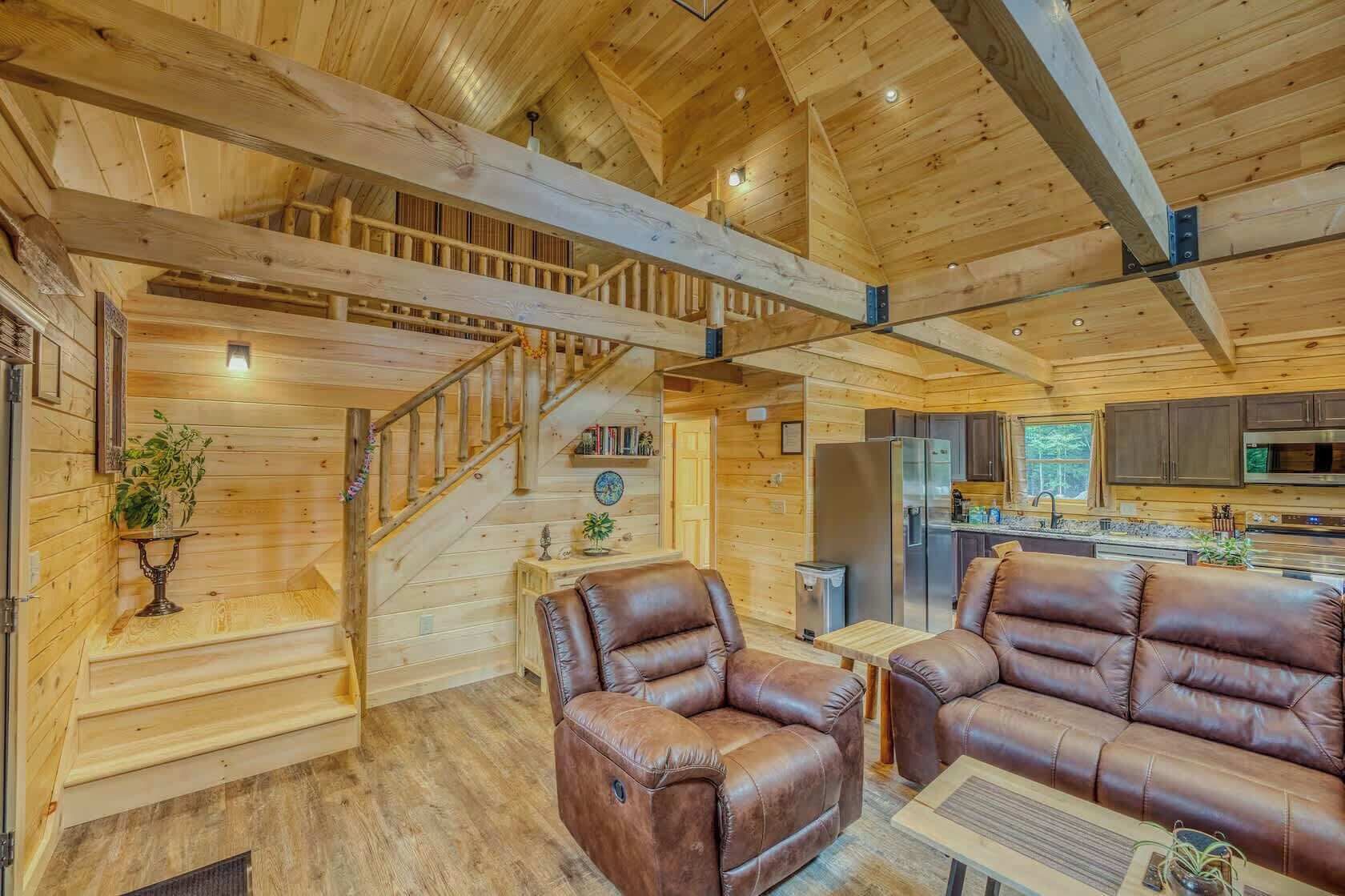 A wooden interior with a staircase, leather sofas, a kitchen area, and a dining table.