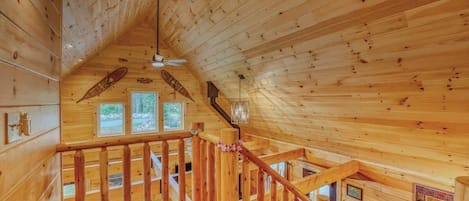 A wooden interior with a staircase, wooden railings, and a ceiling fan.