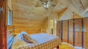 Ein Schlafzimmer in einer Holzhütte mit einem Bett, einem Deckenventilator und einem Fenster.