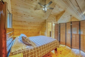 Ein Schlafzimmer in einer Holzhütte mit einem Bett, einem Deckenventilator und einem Fenster.