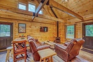 Ein Blockhaus mit Holzvertäfelung, Kamin, Ledersofas, einem Esstisch und Fenstern.