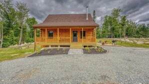 Eine Blockhütte mit Veranda, Schornstein und einem Schotterweg.