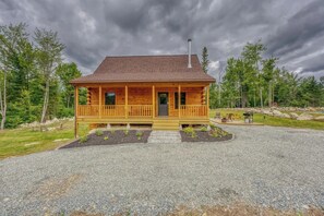 Eine Blockhütte mit Veranda, Schornstein und einem Schotterweg.