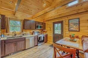 Ein Holzblockhaus-Interieur mit Küche, Essbereich und einer Tür, die nach draußen führt.